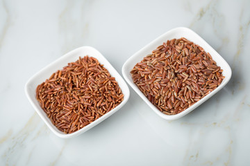 Rotschaliger roher roter Reis aus Piemont Italien und roter Jasmin Reis aus Kambodscha Asien in Porzellan Schale auf Marmor Hintergrund