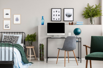 Branches of spruce in glass vases in classy bedroom and workspace for teenager, real photo with posters on empty grey wall