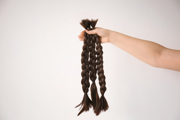 Female hand with braided strands on light background. Concept of hair donation