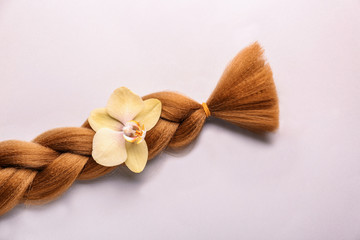 Braided strand and flower on light background. Concept of hair donation