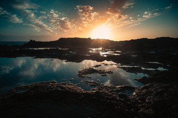 Scenic landscape sunset on he ocean with rocks and clouds - sun light and vacation concept - blue water and orange sky