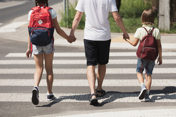 Responsible parent holding hands of children while walking through crosswalk - obrazy, fototapety, plakaty