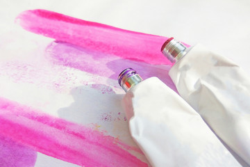 Pink watercolor and acrylic paints tubes and hand drawn abstract magenta watercolour drawing picture on white textured paper background
