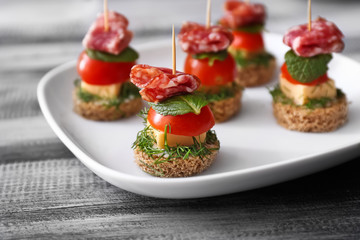 Plate with tasty canapes on wooden table