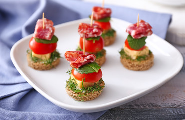 Plate with tasty canapes on wooden table