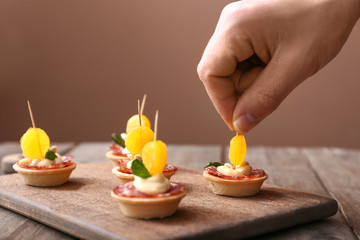 Obraz na płótnie Canvas Female hand with tasty canapes on wooden board