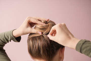 Young woman doing hair on color background