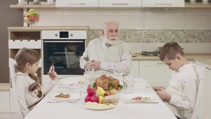 Fototapeta na wymiar Grandpa Communicates With Grandchildren At The Table Before A Family Dinner