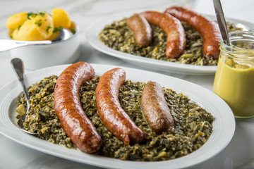 Norddeutscher Grünkohl und regionale Kohlwurst Variation aus Bremer, Oldenburger und Ammerländer Pinkel auf Platten mit Kartoffeln und Senf auf Marmor Tisch