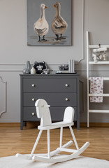 White rocking horse on rug in grey kid's room interior with ladder and poster above cabinet. Real photo