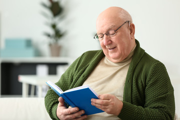 Senior man with hearing aid reading book at home