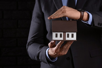 Insurance agent with model of house on dark background, closeup. Protection of house from earthquake