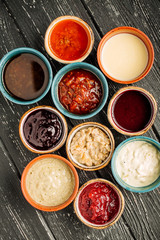 Set of different sauces on black wooden background.