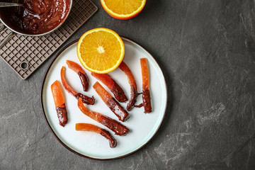 Plate with tasty chocolate covered orange peels on dark table