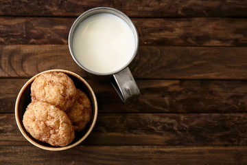 Bowl with tasty cookies and cup of milk on wooden table