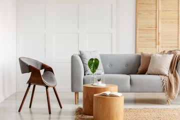 Real photo of a natural living room interior with an armchair, sofa and wooden accents