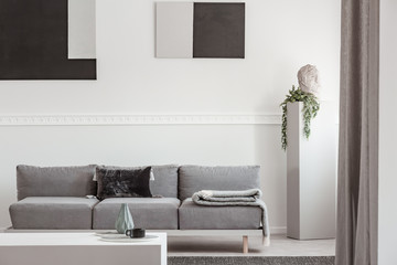 Flowers in vase on coffee table in front of grey Scandinavian couch with pillows