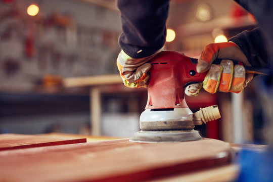 Male carpenter using orbital electric sander in a retro vintage workshop.