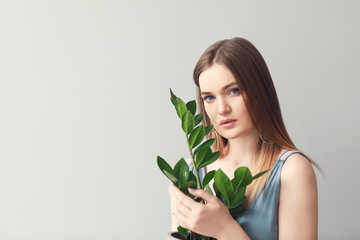 Portrait of beautiful woman with green tropical plant on light background