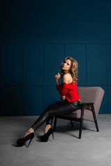 Sensual blonde girl with lush curly hair wearing lace blouse and leather trousers, posing at studio