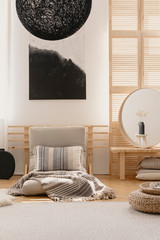 Abstract black and white painting on the wall in bright bedroom interior with futon bed and mirror on bedside table