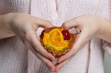 Female hands holding yummy cupcake with berries and orange and making heart shape