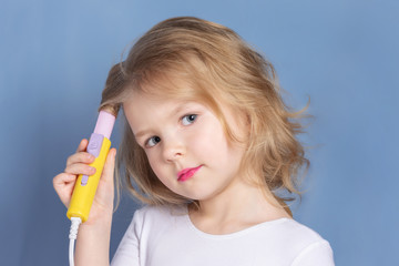 Little girl with blond hair makes styling. The child is holding curling irons. Bright advertising photography.