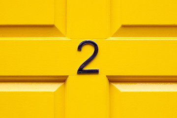 House number two with the 2 in the middle cross bar of a bright yellow painted house door