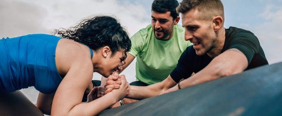 Female participant in an obstacle course climbing a drum helped by her teammates