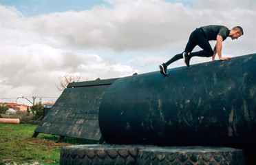 Male participant in an obstacle course climbing a drum