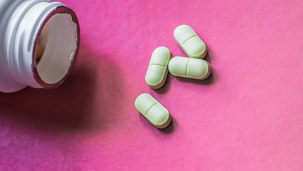 White, green, pink, orange capsules pill spilled out from white plastic bottle container. Global healthcare concept. Antibiotics drug resistance. Antimicrobial capsule pills and thermometer. Pharmaceu