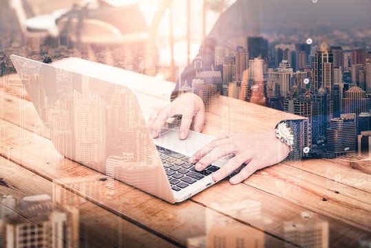 The double exposure image of the business man using a laptop computer during sunrise overlay with cityscape image. The concept of modern life, business, city life and internet of things.