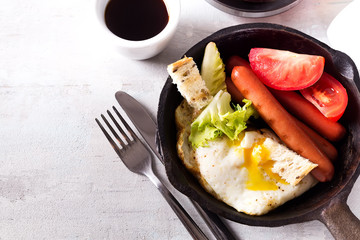 English breakfast in pan with fried eggs, sausages, toasts, vegetables and coffee on light stone background, flat lay