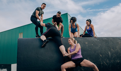 Group of participants in an obstacle course helping a teammate to climb a drum