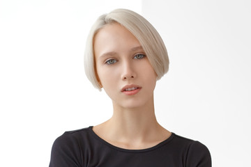 Portrait of young girl with blond short hairstyle looking at camera. Fashion blonde wearing a black...