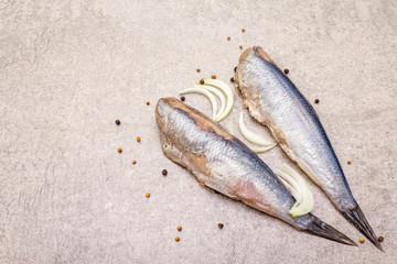 Traditional Norwegian herring "Matias Queen", whole carcasses. Ingredient for smorrebrod, snacks, antipasti. With sliced onion, black pepper, coriander. On stone background, copy space.