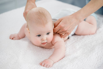 Mother's hands massage the muscles of the back of her baby. Preventive gymnastics. Light background