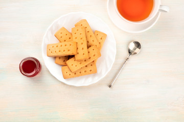 A closeup photo of Scottish shortbread butter cookies, shot from the top with a cup of tea, a jar of jam, and a place for text
