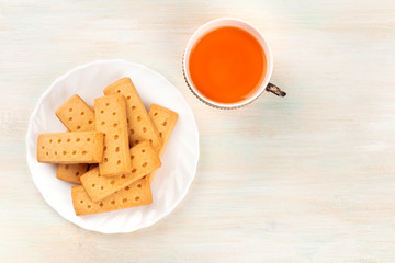 A photo of Scottish shortbread butter cookies, shot from the top on a white wooden background with a cup of tea and copy space