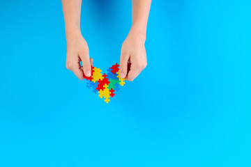 Child hand holding colorful heart on blue background. World autism awareness day concept