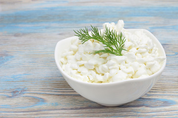 Fresh natural cottage cheese in a white ceramic bowl on the blue wooden table. Green dill. Organic eco healthy meal, dairy product.