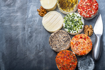 Assortment of French fresh white soft goat cheeses with different tastes topping made with herbs, paprika, indian curry, bruscetta, chives and dried tomatoes
