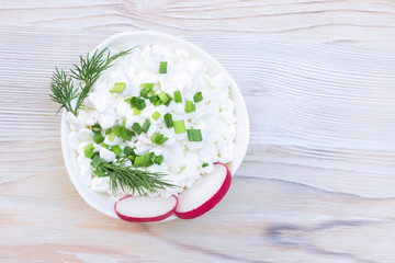 Fresh natural cottage cheese in a white ceramic bowl on the vintage wooden table. Green dill. Organic eco healthy meal, dairy product. Top view, overhead photo with place for text, copyspace.