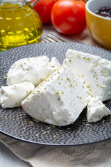 Fresh young soft white Feta cheese on black plate seasoned with dried oregano herb