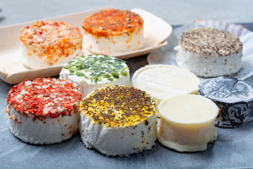 Assortment of French fresh white soft goat cheeses with different tastes topping made with herbs, paprika, indian curry, bruscetta, chives and dried tomatoes