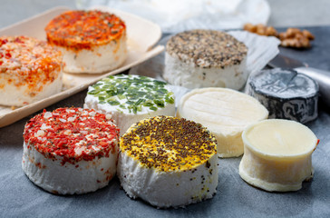 Assortment of French fresh white soft goat cheeses with different tastes topping made with herbs, paprika, indian curry, bruscetta, chives and dried tomatoes