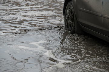 Poor road condotions - car wheel in melting show puddle.