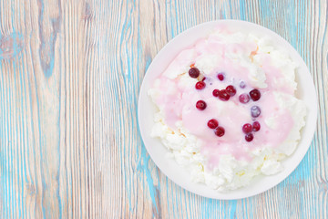 An overhead photo of fresh natural cottage cheese with cranberry yogurt in a white ceramic bowl on the wooden table. Organic eco healthy meal, dairy product. Top view. Place for text, copyspace.