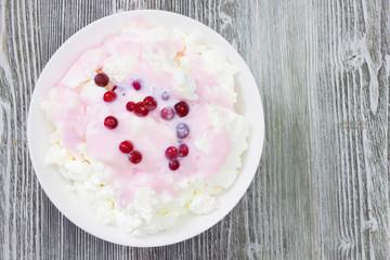 An overhead photo of fresh natural cottage cheese with cranberry yogurt in a white ceramic bowl on the wooden table. Organic eco healthy meal, dairy product. Top view. Place for text, copyspace.