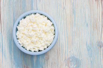 An overhead photo of fresh natural cottage cheese in a blue ceramic bowl on the wooden table. Organic eco healthy meal, dairy product. Top view Place for text, copyspace.